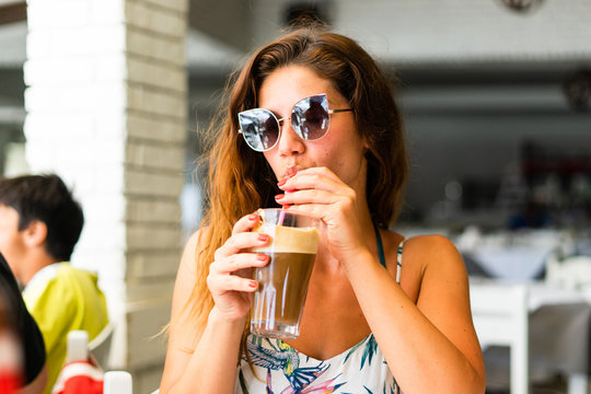 Portrait of young woman at the restaurant drinking frappe coffee in a summer day on the vacation wearing sunglasses