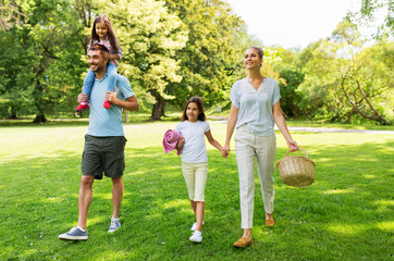 Fototapeta premium family, leisure and people concept - happy mother with picnic basket, father and two daughters walking in summer park