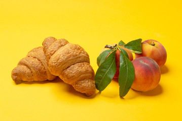 French croissants and fresh peaches on yellow background close up. Summertime meal	