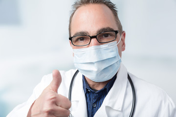 doctor with medical face mask and stethoscope shows thumbs up