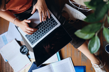 Close up student girl sitting on floor working on laptop with cup of coffee to go and textbooks...