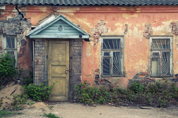 Facade of an old abandoned house. Wooden entrance door, windows, shabby plastered brick walls. Close-up view, urban background