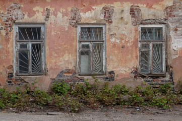 Fototapeta na wymiar Close-up view of the facade of an old abandoned house. Three windows with lattice, shabby plastered brick walls. Urban background