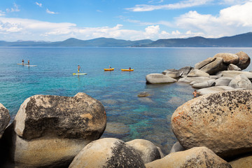 Kayakers and paddleboarders paddling on the turquoise crystal-clear water of Sand Harbor in Lake...