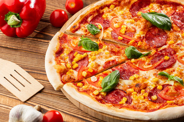 Delicious hot homemade pizza on the wooden table. Pizza - Fresh homemade pizza with pepperoni, cheese and tomato sauce, tomatoes, sweet corn and basil with copy space.