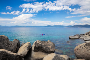 Fototapeta na wymiar Tandem kayak in the middle of beautiful blue water of Lake Tahoe with boulders in the foreground