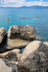 Colorful kayakers and paddle boarders paddling on crystal clear water of Lake Tahoe with massive...