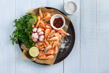 Raw prawns in a cooking pan with ingredients for preparation fried shrimps on blue wooden background with copy space top view