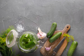 Pickling and fermentation cucumber in glass jar with dill and garlic on dark grey concrete table. Top view with copy space.