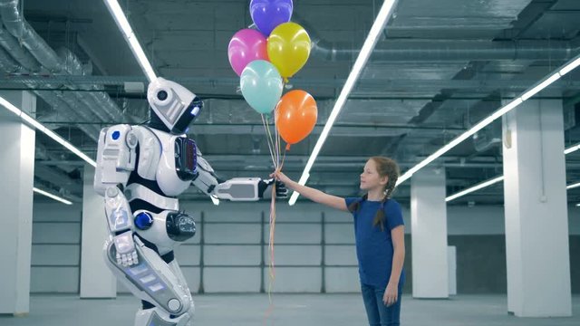 Modern robot gifts balloons to a little girl, side view.