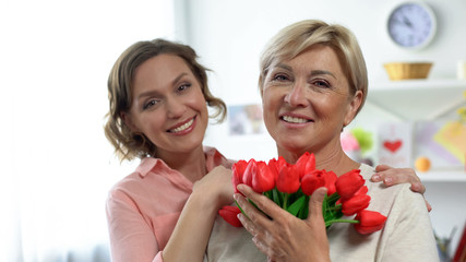 Pretty daughter and mom with tulips smiling at camera, mothers day celebration
