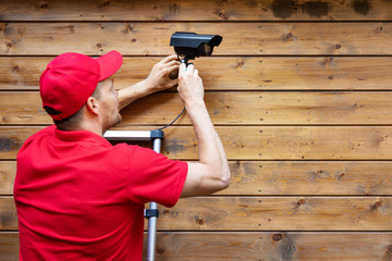 home security - man installing outdoor surveillance camera on wooden wall copy space