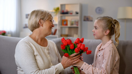 Pretty girl giving red tulips to grandmother, family love, birthday celebration