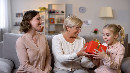 Obraz na płótnie Canvas Grandmother and daughter giving present to schoolgirl, motherhood care, love
