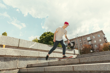 Skateboarder doing a trick at the city's street in sunny day. Young man in sneakers and cap riding...