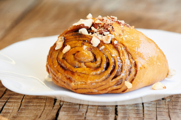 Appetizing cinnamon roll on a white plate. Homemade pastry, bun with nuts topping
