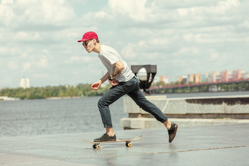 Skateboarder doing a trick at the city's street in sunny day. Young man in sneakers and cap riding...
