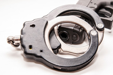 A set of black and silver handcuffs on top of a black 9mm pistol on a white background