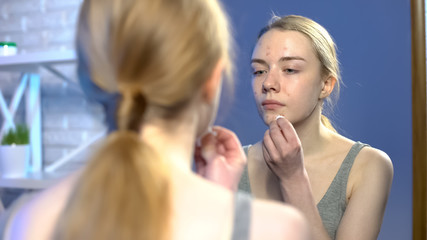 Obraz na płótnie Canvas Teenage girl in puberty age cleaning face with tonic lotion, applying acne cream