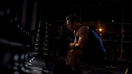 Fototapeta na wymiar Strong bodybuilder resting after intensive workout with dumbbells at the gym