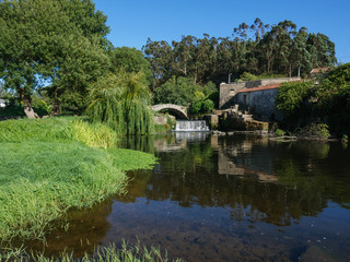 Fototapeta premium Beautiful scenic view over river Este in Portugal, on a sunny summer day with blue sky. Old stone bridge, ruin of stone house, and overhanging willow tree on bank.