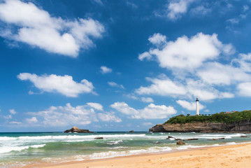 Naklejka premium Beach in Biarritz city with the lighthouse and white clouds on a polarised blue sky. Basque coast of France.