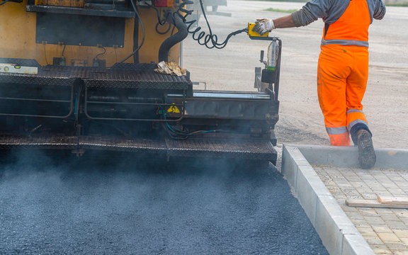 Workers regulate tracked paver laying asphalt heated to temperatures above 160 ° pavement on a runway