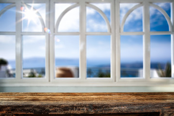 Fototapeta premium Table background with wooden top board and white window. Beautiful blurred ocean and beach view outside the window.