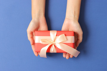 gift in female hands on a colored background top view.