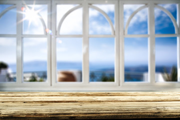 Fototapeta premium Table background with wooden top board and white window. Beautiful blurred ocean and beach view outside the window.