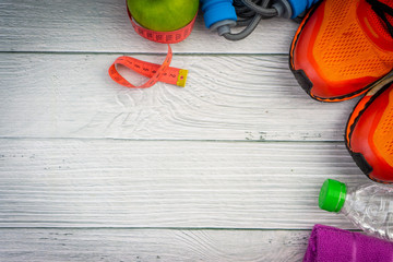 Top or flat lay view of towel, water, apple fruit, sport shoes and skipping rope with copy space area on wooden background. Healthy concept. Selective focus.