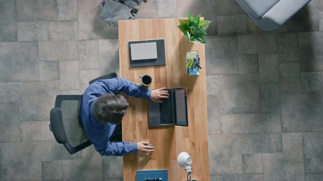 In the Office Businessman Sitting at the Wooden Desk Opens Laptop and Starts Working He Drinks Coffee, Types, Writes Emails, Surfs the Internet, Designs Software