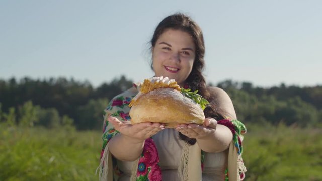 Portrait of cute plump woman proposing lard on the loaf of white bread smiling looking at the camera. Hospitality concept. Real rural woman.
