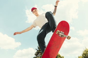 Skateboarder doing a trick at the city's street in sunny day. Young man in sneakers and cap riding...