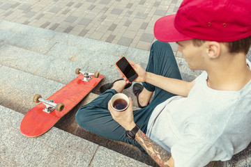 Skateboarder preparing for riding at the city's street in sunny day. Young man in sneakers and cap with a longboard on the asphalt. Concept of leisure activity, sport, extreme, hobby and motion.