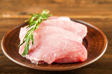 Meat fillet in a plate with rosemary, peppercorns close-up. Chicken, turkey, pork, beef fillet in a plate on a textured wooden table, copy space.
