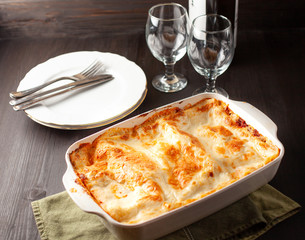 Homemade lasagna in a white bowl with cutlery in the background