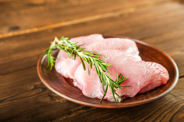 Meat fillet in a plate with rosemary, peppercorns close-up. Chicken, turkey, pork, beef fillet in a plate on a textured wooden table, copy space.