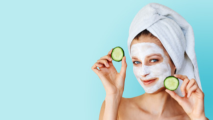 Beautiful young woman with facial mask on her face holding slices of cucumber. Skin care and...