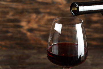 red wine pour into a glass on a wooden background, space for text.