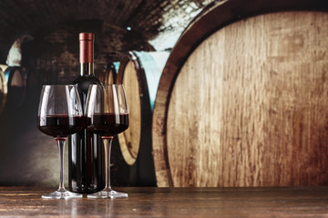 red wine in a glass on the background of barrels in the cellar - obrazy, fototapety, plakaty