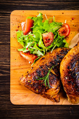 Roasted chicken leg with french fries and vegetable salad on wooden background