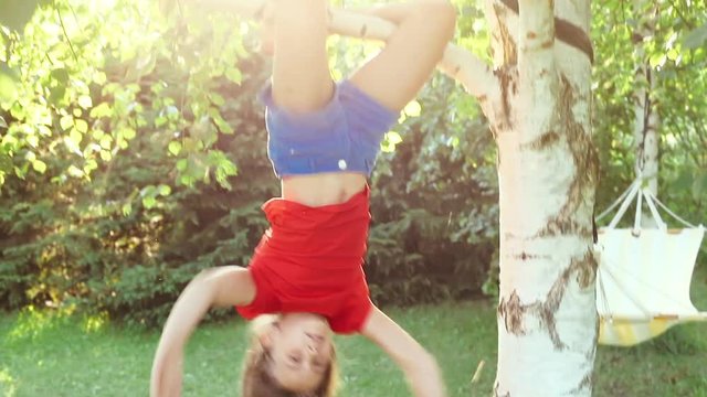 Happy little girl hanging from a tree playing in a sunny backyard summer fun concept_9808