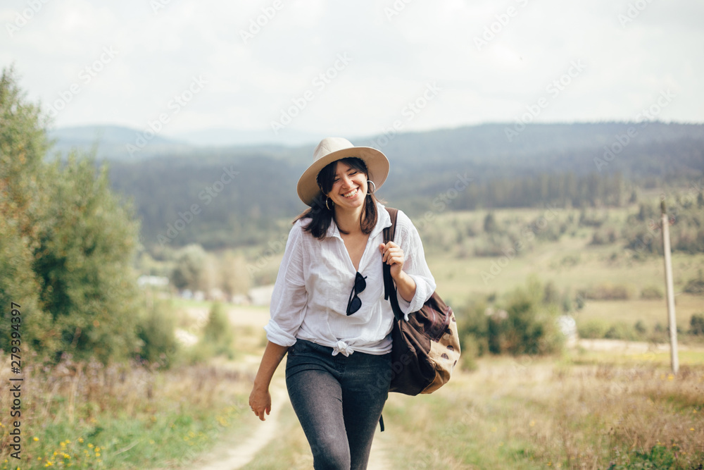 Wall mural happy hipster girl with backpack traveling on top of sunny mountain, walking on hills with woods. st