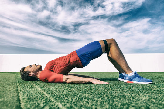 Resistance Band Training Fit Man Doing Bridge Exercise Fitness Athlete Doing Glute Workout Outside On Grass.