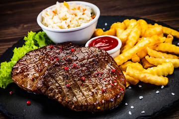 Grilled steak with french fries and vegetables served on black stone on wooden table