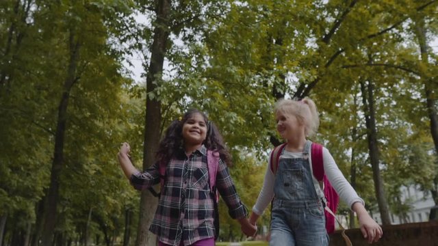 Three Friends With Backpacks Are Going to School. Mixed Racial Group of School Kids Walking in the Park holding hands. Slow Motion Shot.