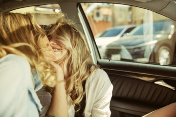 Fototapeta na wymiar Young lesbian's couple kissing before vacation trip on the car in sunny day. Women sitting and ready for going to sea, riverside or ocean. Concept of relationship, love, summer, weekend, honeymoon.