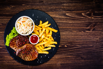 Grilled steak with french fries and vegetables served on black stone on wooden table