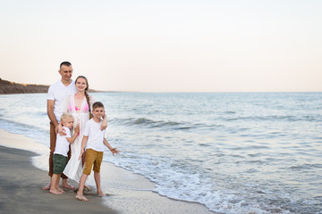 Happy family of four hugging on the sea coast. Parents, pregnant mother and two sons.